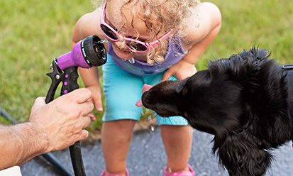 Kind und Hund die aus dem Gartenwasserschlauch trinken
